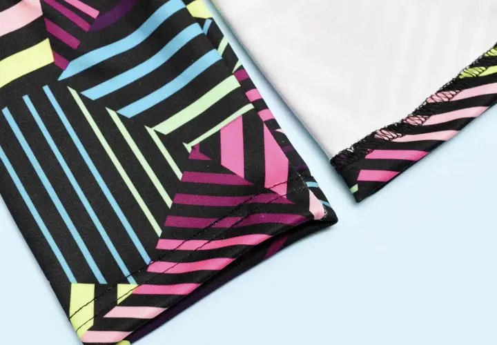 Close-up of colorful geometric leggings. The fabric is black with vibrant stripes of pink, blue, yellow, and green. The stitching shows how you can sew leggings.