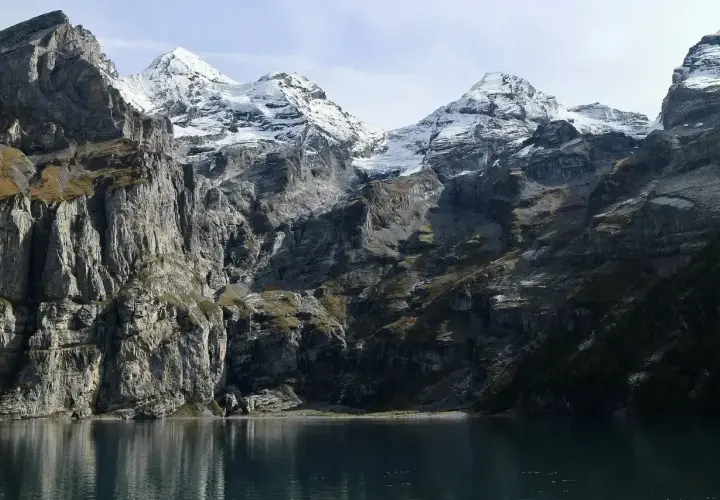 Majestatyczny łańcuch górski z ośnieżonymi szczytami, przypominający Tatry, odbija się w spokojnej tafli jeziora.