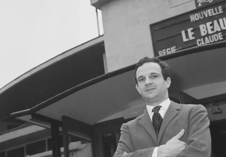 Jean Pierre Léaud w garniturze, z rękami skrzyżowanymi na piersi, przed budynkiem z napisem "Le Beau Serge".