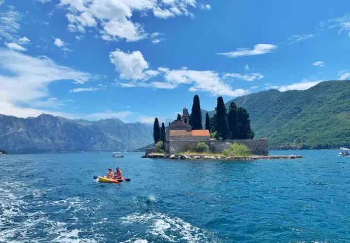 Kayaking in Montenegro's Bay of Kotor, a perfect spot for any trip planner. Mountains and a church on an island create a stunning backdrop.