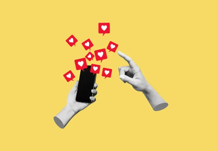 Dwie ręce, jedna trzyma smartfon, druga wskazuje na ekran, z którego wylatują czerwone dymki z serduszkami, symbolizujące polubienia w social mediach.