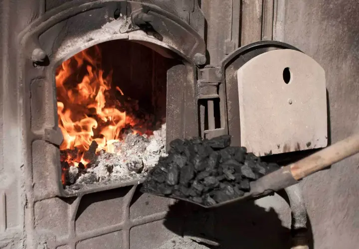 Fachowiec od pieca zasypuje węglem palenisko, gdzie szaleje ogień.