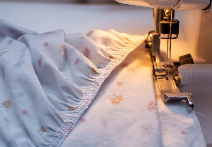 A serger creates a gathered edge on a floral-patterned fabric, preparing it for a sewing project.
