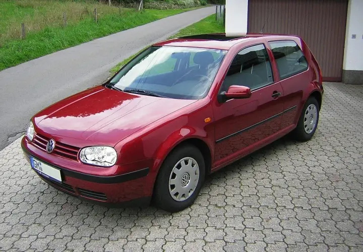 Czerwony Volkswagen Golf IV zaparkowany na podjeździe z kostki brukowej, obok garażu.