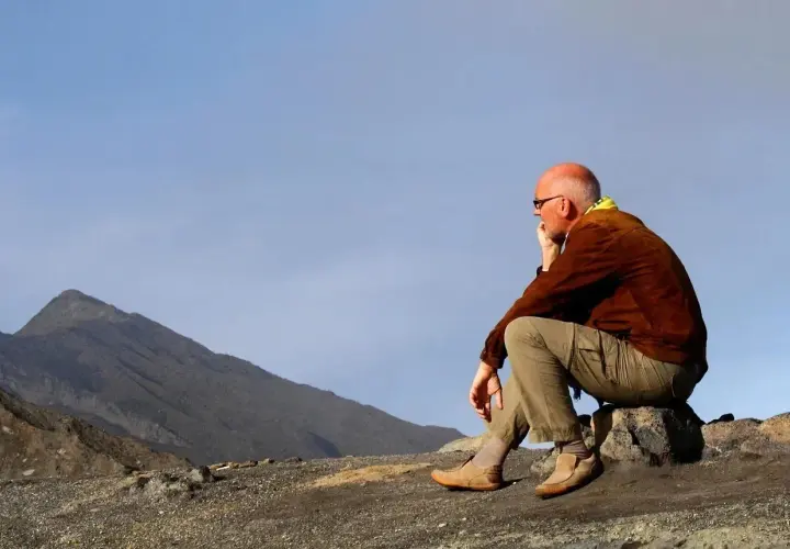 A man in hiking gear sits on a rock, contemplating the vast, barren landscape. This is the essence of zero day hiking, a moment of quiet reflection before the real adventure begins.