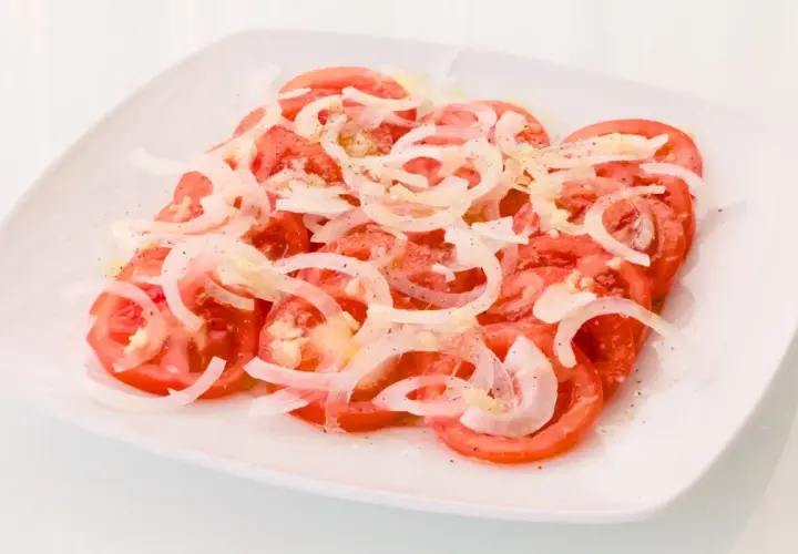 Una refrescante ensalada de tomate y cebolla, aderezada con sal y pimienta, lista para disfrutar.