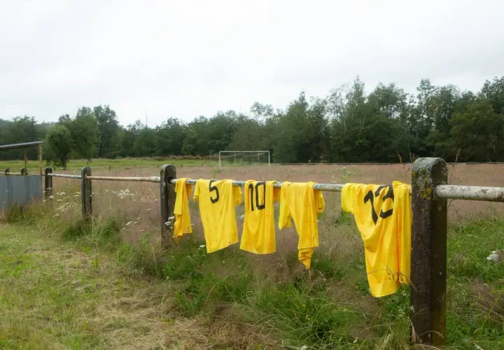 Maillots de foot jaunes floqués, numéros 5, 10, 12, sèchent sur une barre rouillée. Une astuce pour savoir comment laver un maillot de foot floqué.