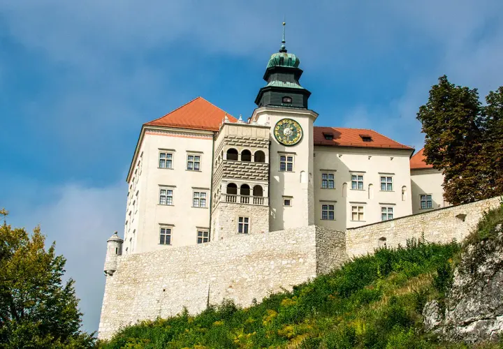Zamek na Pieskowej Skale, biały z czerwonym dachem, z wieżą zegarową, na tle błękitnego nieba.