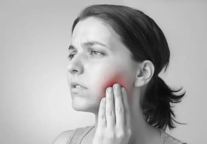 Mujer con dolor en la mejilla, indicando un posible flemón por muela del juicio.