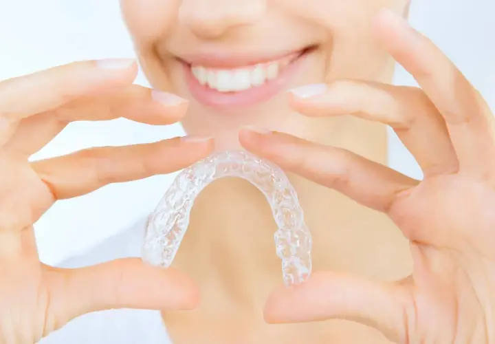 Manos sostienen un alineador transparente, mostrando cómo quitar Invisalign para una sonrisa perfecta.
