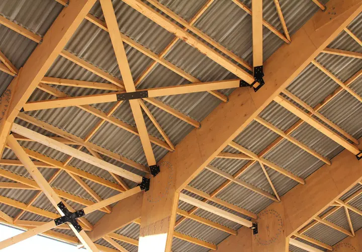 Structure complexe de poutres en bois de type **lvl bois**, soutenant un toit ondulé.