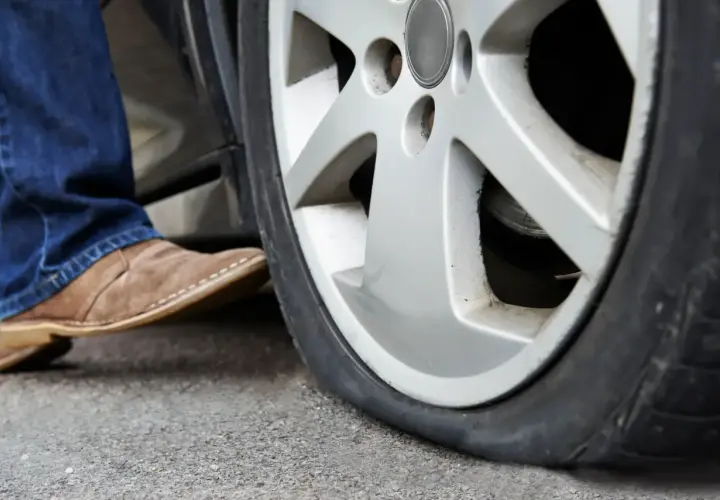 Un neumático pinchado, ¿qué es un runflat? Un pie con zapato de gamuza se acerca a la rueda desinflada.