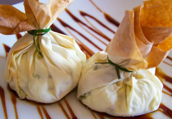 Dos saquitos de pasta filo rellenos, atados con hilo verde, reposan sobre un plato con un glaseado oscuro.