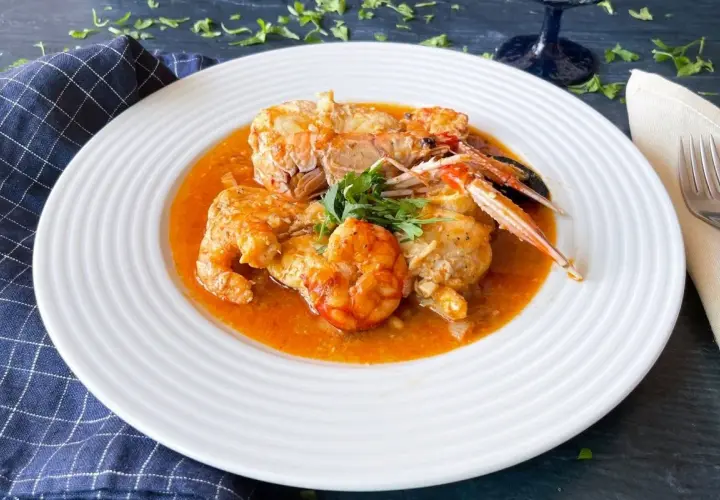 Rape en salsa con gambas y cigalas, servido en plato blanco con perejil fresco.