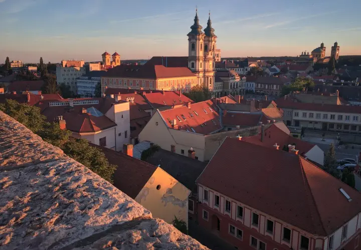 Widok na Eger z zamku o zachodzie słońca. Czerwone dachy, barokowa bazylika i wieże kościelne w złotym blasku.
