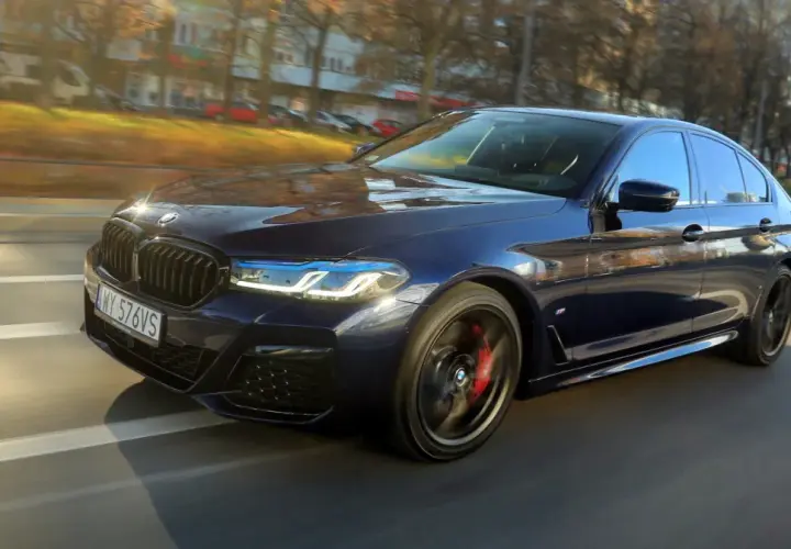 Ciemnoniebieskie BMW 540d sunie po drodze, odbijając jesienne słońce.