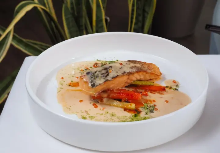Un filet de poisson poêlé, baignant dans une onctueuse sauce champagne, accompagné de légumes croquants et de quelques perles orangées.
