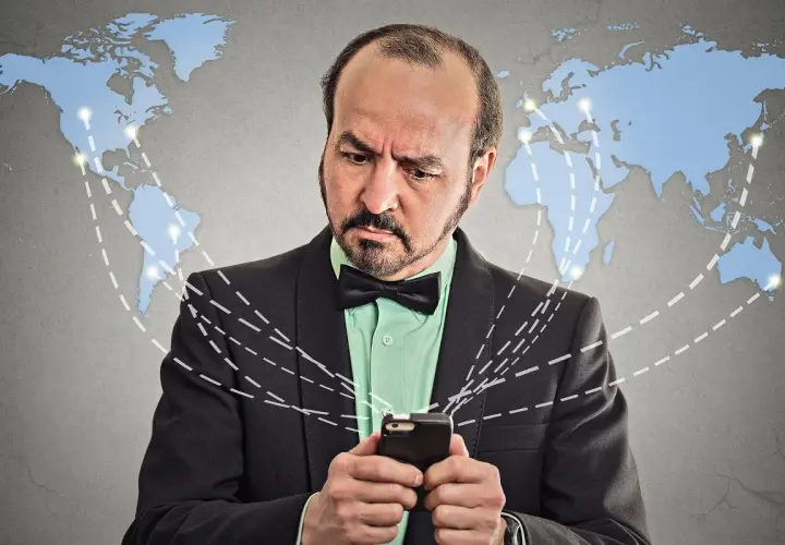 Mężczyzna zamyślony nad telefonem, szukający informacji, jak aktywować roaming w Orange, na tle mapy świata z połączeniami.