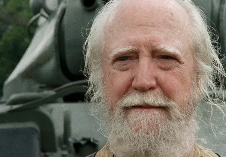 Hershel Greene, członek obsady "Żywych trupów", z siwą brodą i włosami, na tle pojazdu.