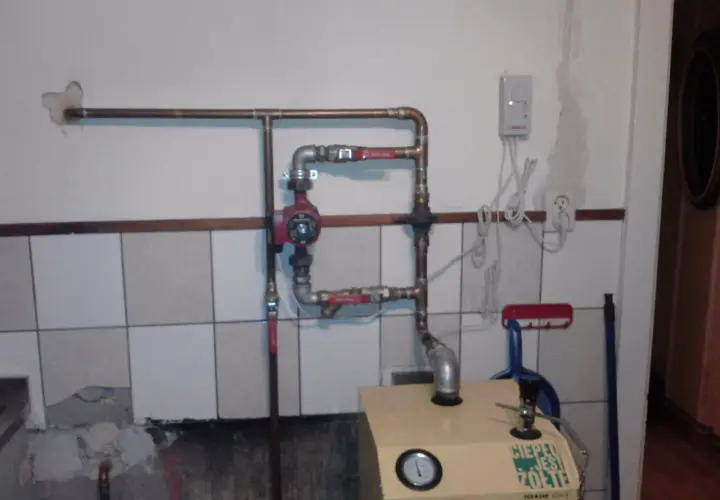 Montaż pompy CO w układzie otwartym. Widoczna instalacja hydrauliczna, czerwona pompa, zawory i fragment kotła.