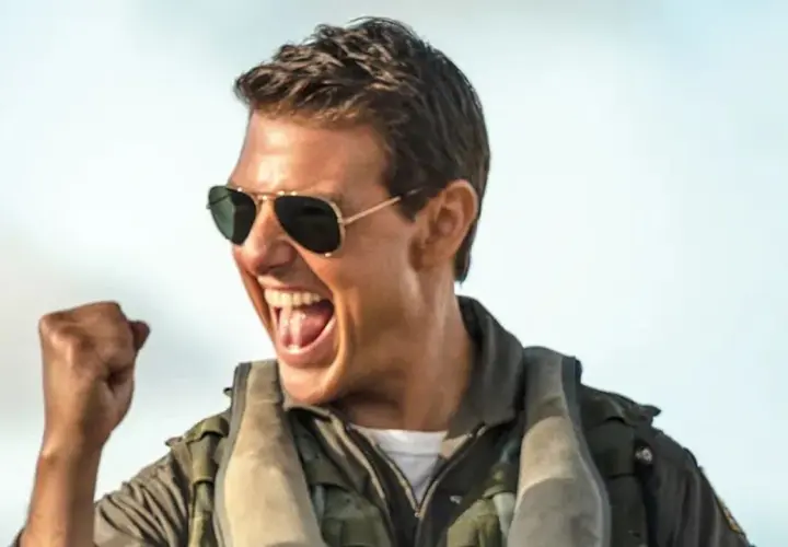 Tom Cruise w okularach przeciwsłonecznych i kurtce pilota, z zaciśniętą pięścią, krzyczy z radości. Czekamy na **Top Gun 3**!