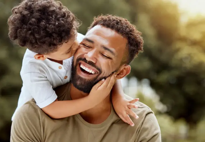 Un niño abraza a su padre, quien ríe feliz. Un momento tierno que inspira frases de padres a hijos para reflexionar sobre el amor.