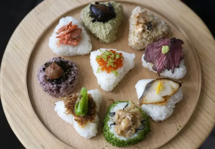 A colorful assortment of Japanese triangle food, including onigiri with salmon, beef, fish, and ikura, arranged on a wooden platter.