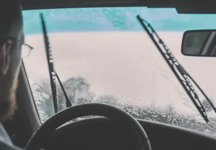 Conductor con gafas y barba, mira a través del parabrisas mojado. ¿Qué hacer si llueve y no anda el limpiaparabrisas?