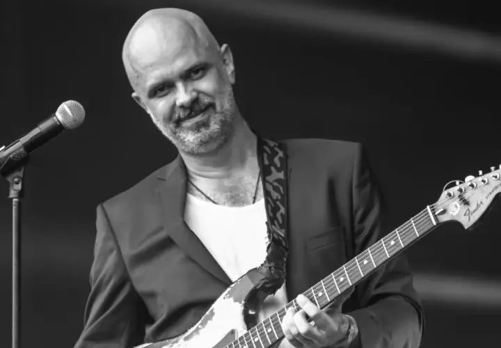 Jacek Budyń Szymkiewicz, w garniturze i z gitarą Fender Stratocaster, gra na scenie.