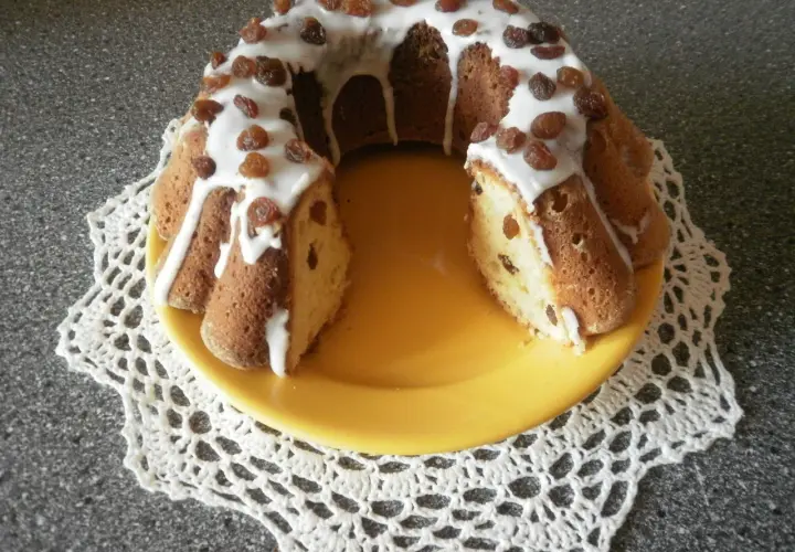 Pyszna babka drożdżowa Ani gotuje, polana lukrem i posypana rodzynkami, na żółtym talerzu.