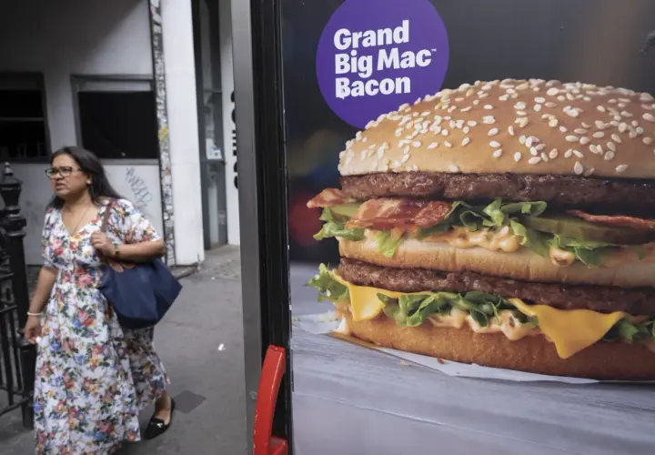 Reklama Grand Big Mac Bacon. Kobieta w kwiecistej sukience mija billboard z apetycznym burgerem.