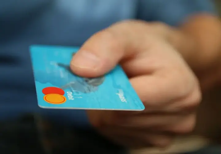 Main tenant une carte bancaire bleue, prêt à effectuer un achat. Il est possible de bloquer un paiement CB en cas de perte.