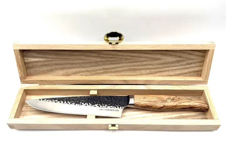 Un magnifique couteau au barbecue, avec une lame martelée et un manche en bois d'olivier, repose dans son coffret en bois.