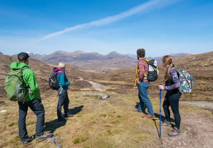 Four hikers enjoy a scenic view on Scotland hiking trips, with mountains stretching into the distance under a clear blue sky.