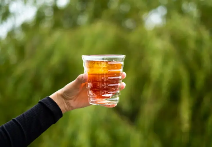 Dłoń trzyma szklankę z bursztynowym napojem, idealnym na orzeźwienie. Zastanawiasz się, jaka kawa do cold brew sprawdzi się najlepiej?