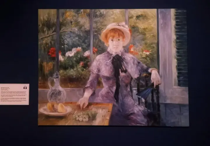 Auguste Renoir dzieła: portret młodej kobiety w kapeluszu, siedzącej przy stole z owocami i dzbankiem, w otoczeniu kwitnącego ogrodu.