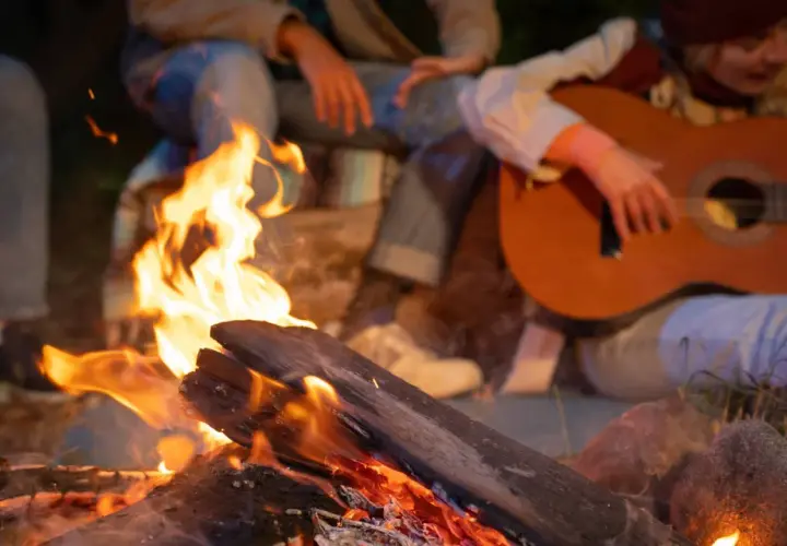 Przy ognisku siedzą ludzie, grają na gitarze i śpiewają piosenki do ogniska.