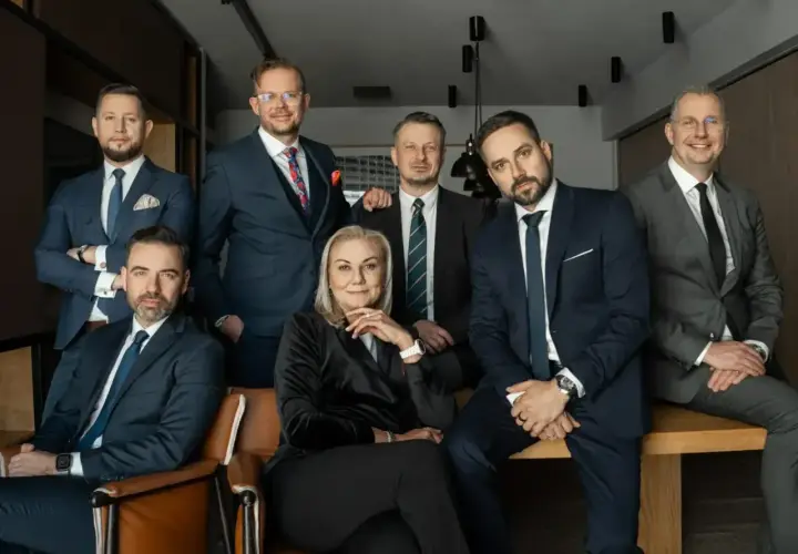 Grupa siedmiu profesjonalistów w garniturach, w tym jedna kobieta, pozuje do zdjęcia.