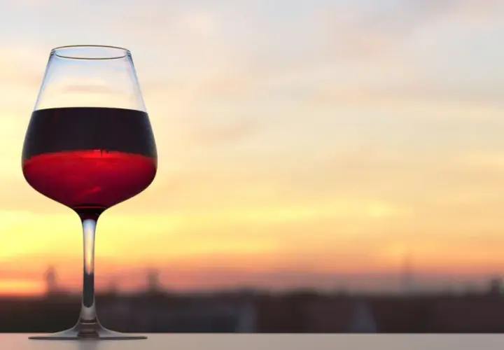 Verre de vin rouge bordeaux, parfait pour apprécier sa température idéale au coucher du soleil.