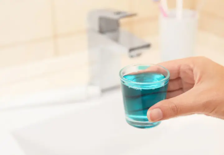 Mano tiene bicchierino con collutorio azzurro, ideale per l'igiene orale in gravidanza.
