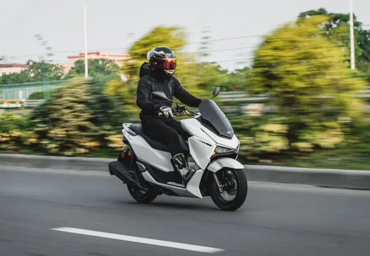 Hombre con casco y chaqueta negra conduce una moto 125 blanca por la autopista, demostrando que una moto 125 puede ir por autopista.