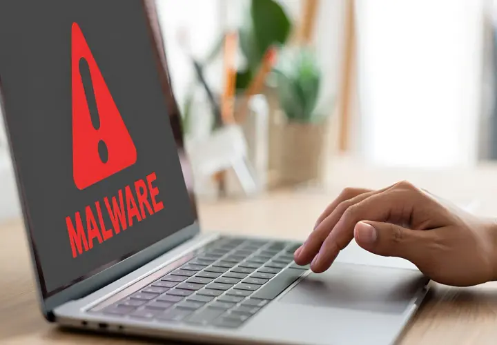 Ostrzeżenie na ekranie laptopa: "MALWARE". Dłoń użytkownika zbliża się do klawiatury, być może próbując dowiedzieć się, spyware co to jest i jak się przed nim chronić.