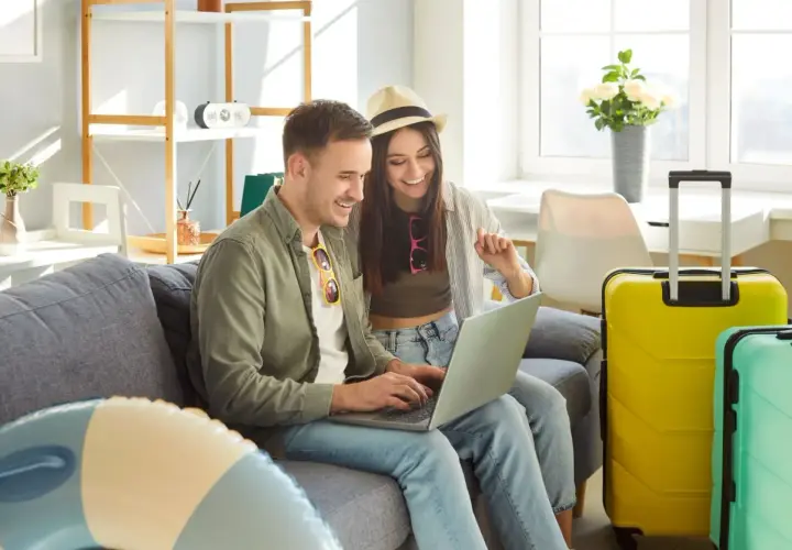 Para, planując kiedy majówka, przegląda oferty wakacyjne na laptopie. Obok walizki czekają na podróż.