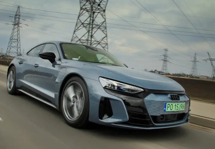 Szary Audi e-tron GT pędzi po drodze, otoczony liniami energetycznymi i słupami wysokiego napięcia.
