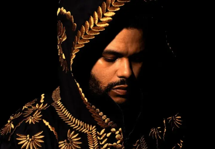 The Weeknd w czarnej, haftowanej złotem bluzie z kapturem, zamyślony. Jego utwory często opowiadają o mrocznych stronach życia.