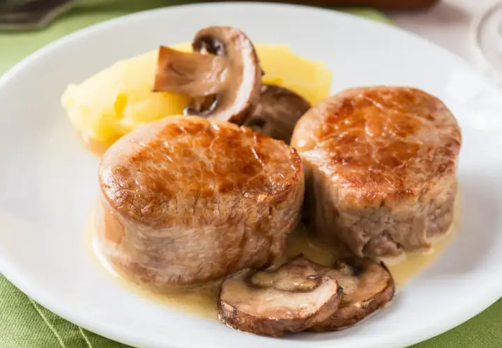 Dwie soczyste polędwiczki wieprzowe w sosie z pieczarkami i puree ziemniaczanym.