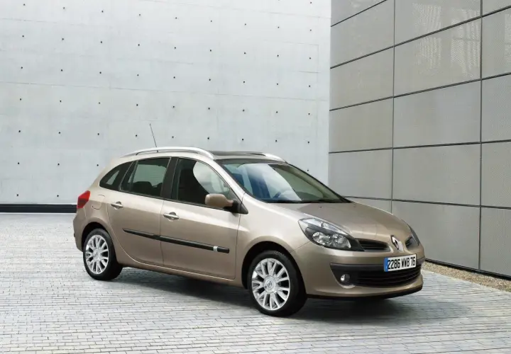 Beżowe Clio 3 kombi stoi na tle nowoczesnego budynku z betonową i metalową elewacją.
