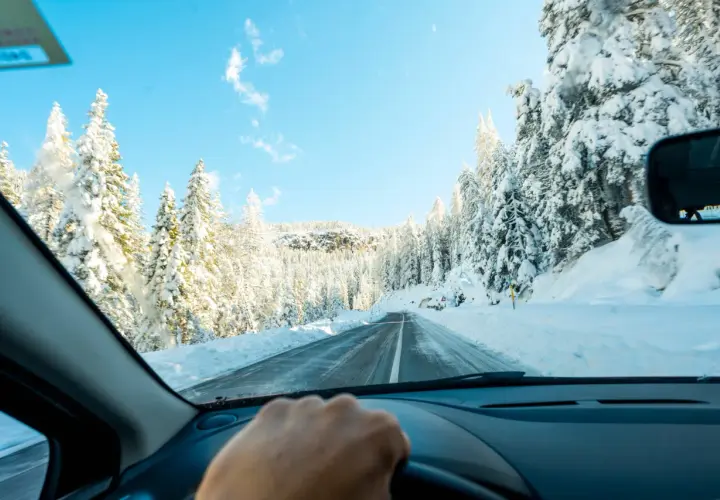 Conduciendo por una carretera nevada, rodeada de árboles cubiertos de blanco. Consejos para como conducir con nieve.