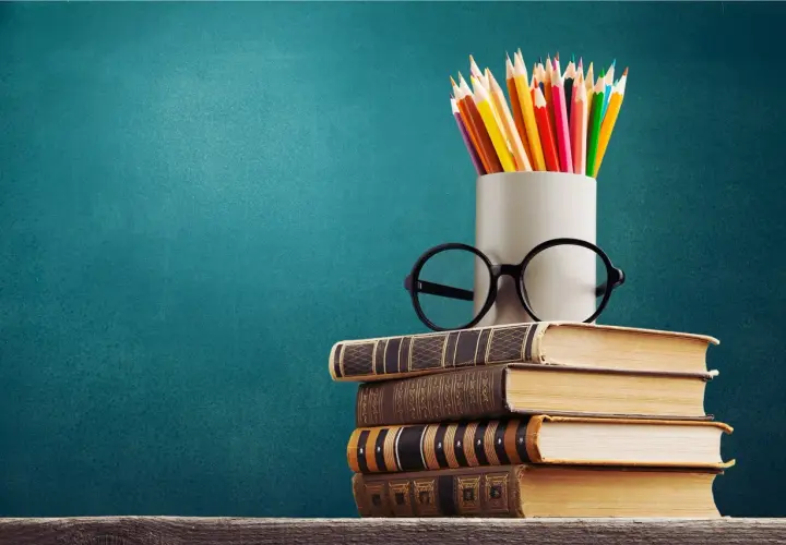 Stos książek, okulary i kredki na tle tablicy. To symbol wiedzy, która otwiera drzwi do kariery, nawet jeśli to co to znaczy wykształcenie średnie branżowe.