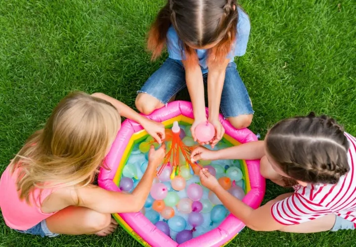 Bambine giocano con palloncini d'acqua in una piscina gonfiabile, perfetti giochi per feste di compleanno 7-8 anni.